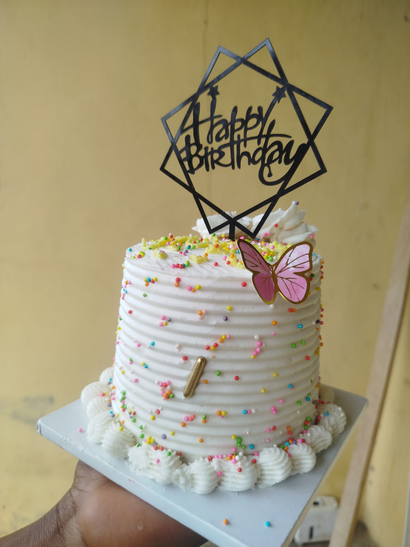 White ridged buttercream cake covered in rainbow sprinkles with a butterfly and Happy Birthday topper