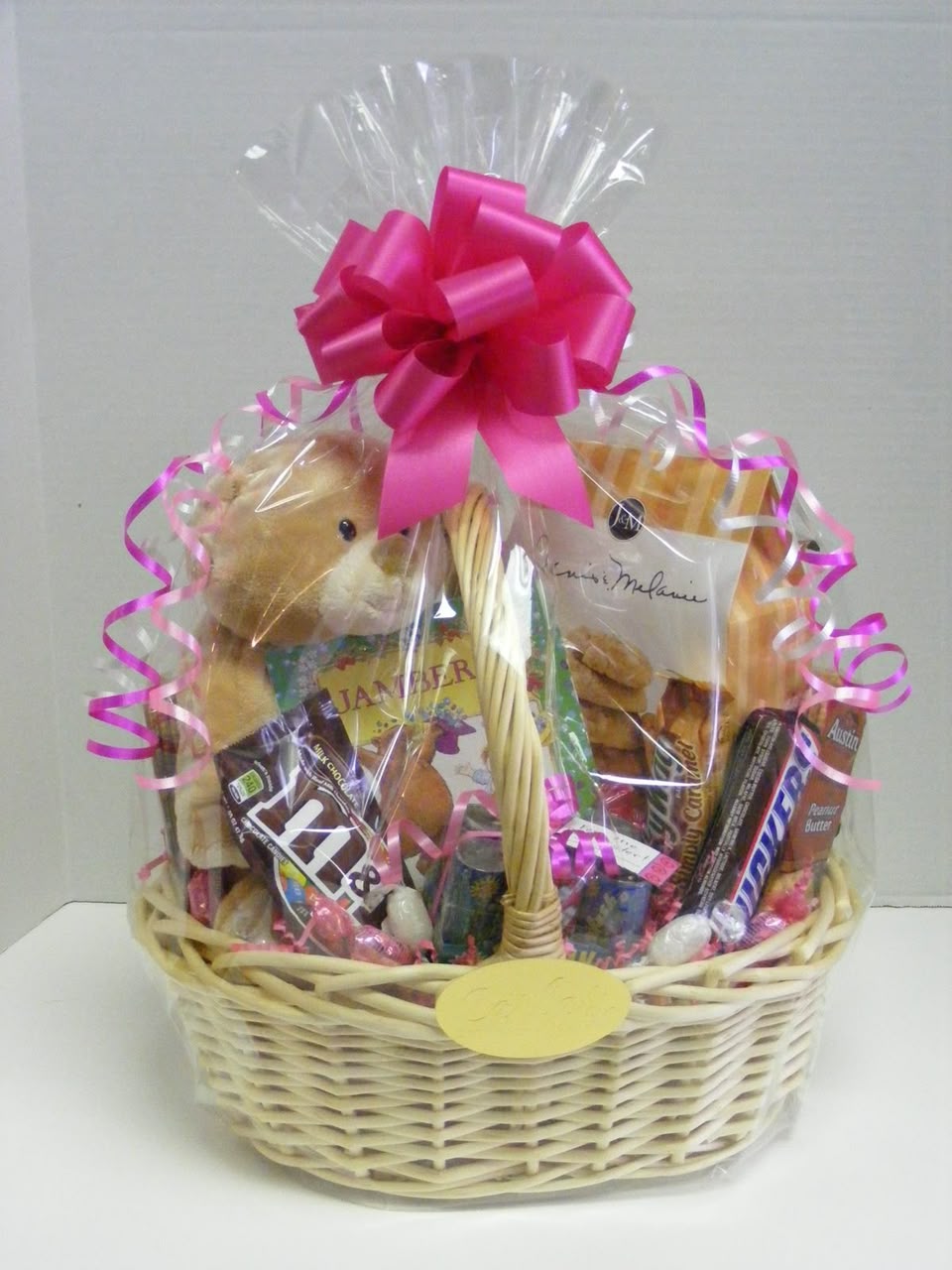 Wrapped celebration gift hamper filled with treats, snacks and a plush bear, finished with a pink bow