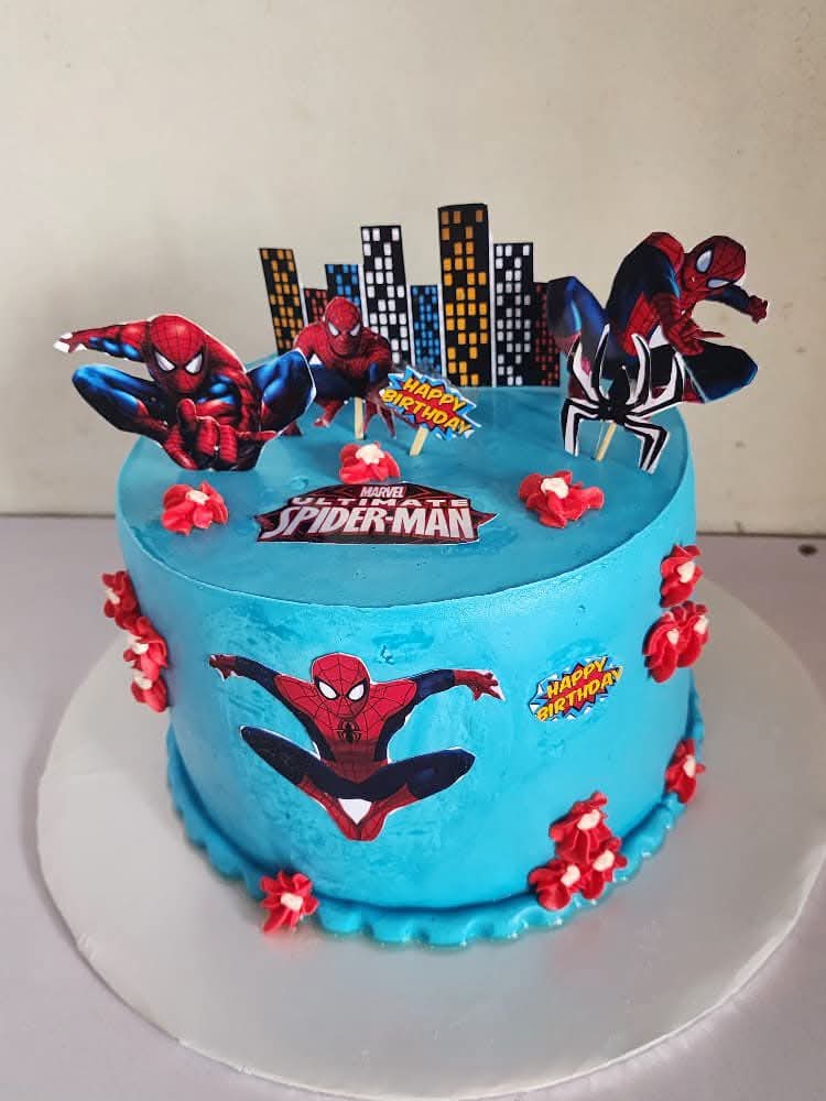 Blue Spider-Man character birthday cake with city skyline toppers and red buttercream flowers