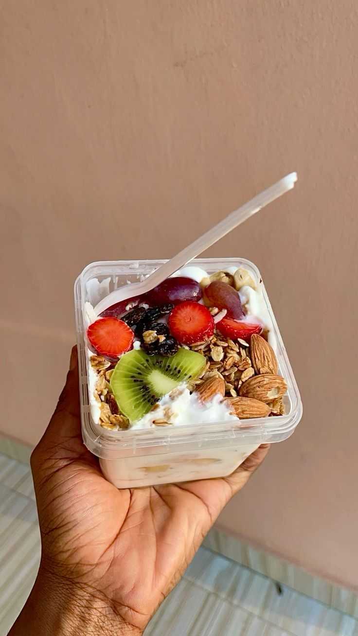 Parfait cup layered with yoghurt, granola, strawberries, kiwi, grapes, raisins and almonds