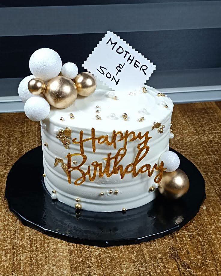 Ivory buttercream cake with gold hand-piped lettering, gold spheres and pearl accents