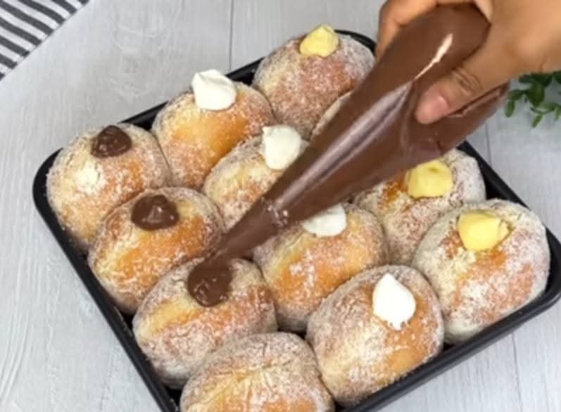 Tray of sugar-dusted bomboloni doughnuts being filled with chocolate, vanilla and custard cream