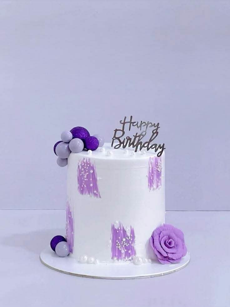 Tall white cake with lilac brushstrokes, sugar pearls, balloon cluster and a purple sugar rose